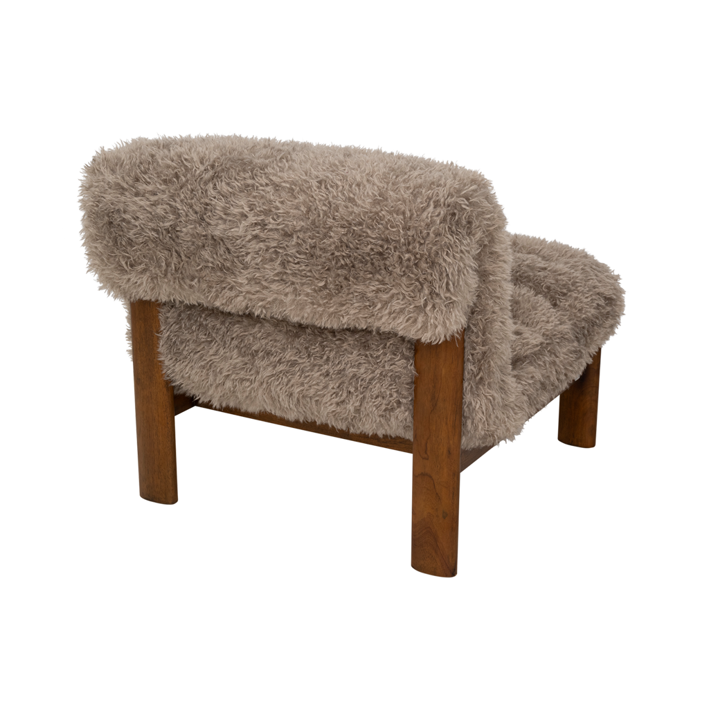 A lounge chair with visible rubber wood legs and a quilted and padded cushioned seat in a draped design. Made from a fluffy poodle fabric in the versatile colour taupe.