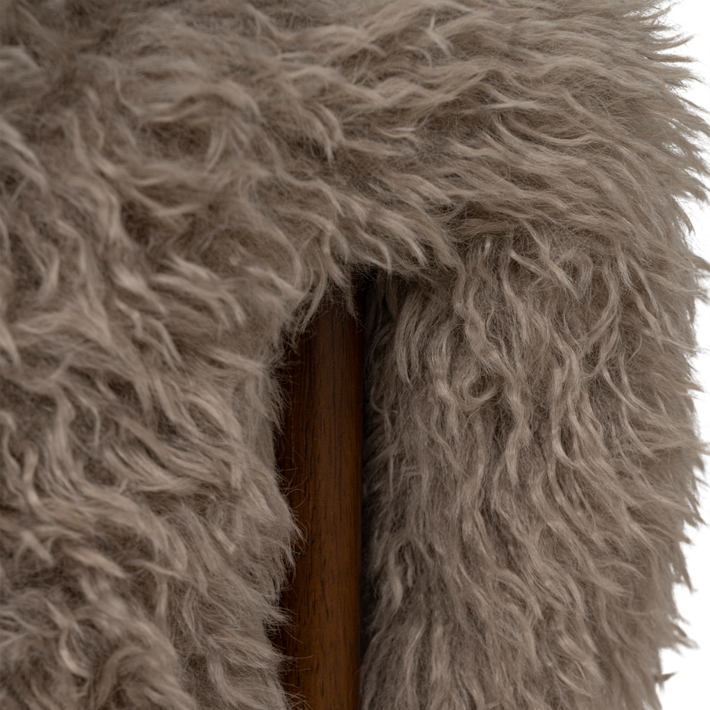 A lounge chair with visible rubber wood legs and a quilted and padded cushioned seat in a draped design. Made from a fluffy poodle fabric in the versatile colour taupe.